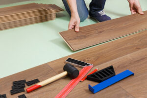 Polaganje laminata s klik sistemom; v ospredju je orodje za montažo.